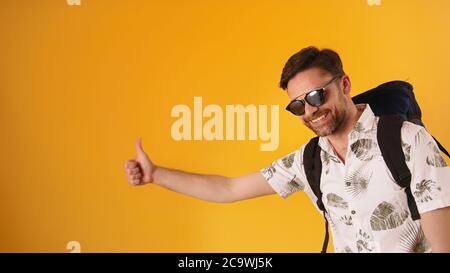 Young bearded man with glasses and backpack holding thumb up, hitchhiking concept. High quality photo Stock Photo