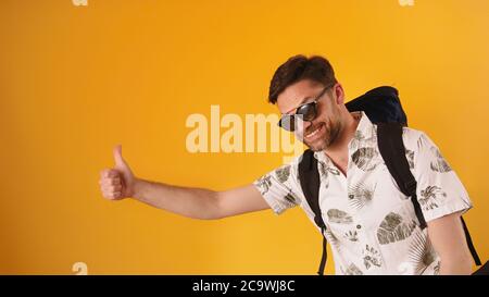 Young bearded man smiling with glasses and backpack holding thumb up, hitchhiking concept. High quality photo Stock Photo