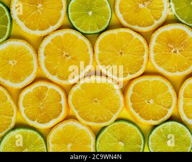Sliced lemons and limes in round slices on yellow background. Top view Stock Photo