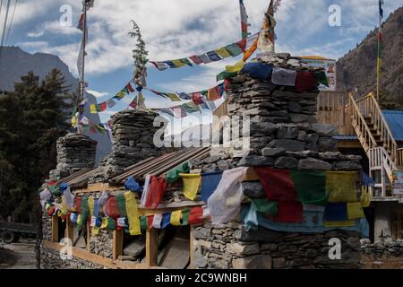 Colorful buddhist prayer flags on stone stupa monument, trekking Annapurna circuit, Himalaya, Nepal Stock Photo