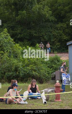 Zinc, Arkansas, USA. 2nd Aug, 2020. Aug. 2, 2020: Protesters eat bbq as militia from the town keep a watchful eye. A variety of groups including Ozarks Hate Watch and Bridge the Gap NWA are marching on Zinc, AR, in a historic march (never before has Zinc had a march of Black groups). Zinc is home of Thomas Robb, who is the grandwizard of the KKK. Credit: Leslie Spurlock/ZUMA Wire/Alamy Live News Stock Photo