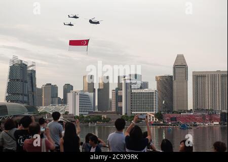 21.07.2018, Singapore, Republic of Singapore, Asia - Spectators observe helicopters of the Singapore Air Force (RSAF) carrying a huge national flag. Stock Photo