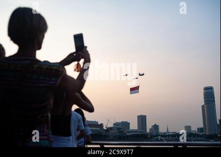 21.07.2018, Singapore, Republic of Singapore, Asia - Spectators observe helicopters of the Singapore Air Force (RSAF) carrying a huge national flag. Stock Photo