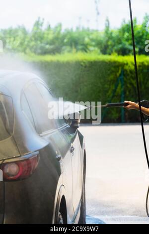 Car's right side being washed with a high pressure water spray wand on an out of focus background. Car washing and cleaning concept. Stock Photo