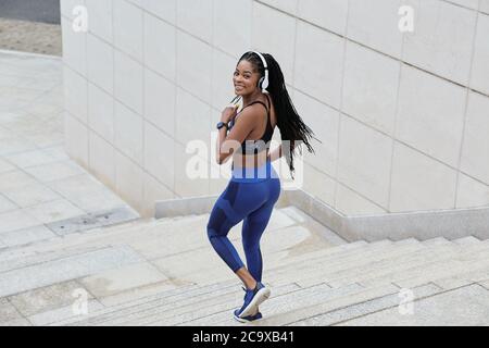 Attractive smiling young Black woman in top and leggins running down the stairs and turning back to camera Stock Photo