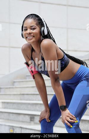 Pretty smiling young mixed-race sportswoman leaning on her laps and looking at camera Stock Photo