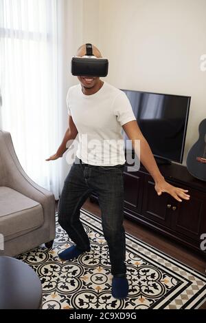 Joyful smiling young Black man testing new virtual reality game when staying home due to lockdown Stock Photo
