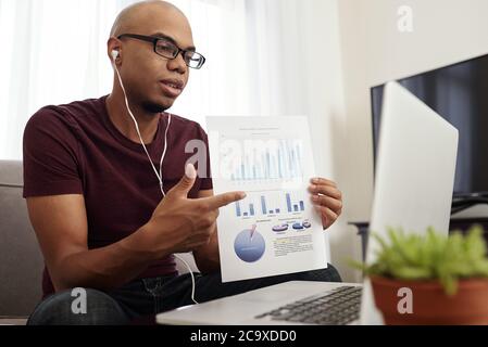 Young African-American financial analyst showing report to colleagues during online conference Stock Photo