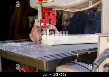 Close-up worker hands in the carpentry workshop cuts the log into boards using band saw. Raw wood and wooden crafts. Stock Photo