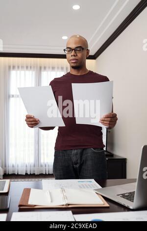 Serious young entrepreneur comparing data in two docuemnts with financial reports Stock Photo