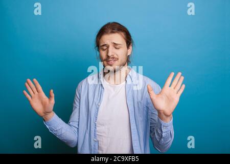 Caucasian man with beard and long hair gesturing the stop sign with palms on blue studio wall Stock Photo