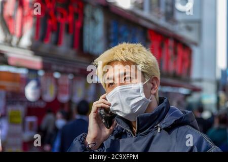 Tokyo, Japan. 27th Feb, 2020. A man with hair dyed blonde wears a face mask as a preventive measure on the street amid coronavirus crisis.The two-month long state of emergency declared by the Japanese government in response to the COVID-19 pandemic ended on June 1st. Despite Japan appearing to have avoided the high infection and mortality rates of some countries during the first wave of the crisis, many areas in Tokyo and across the country have seen businesses shuttered and closed, the cancelling of the 2020 Tokyo Olympics and increasing numbers of infections as people went back to more n Stock Photo