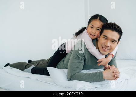 Cheerful Asian girl lying on father's back looking at camera Stock Photo