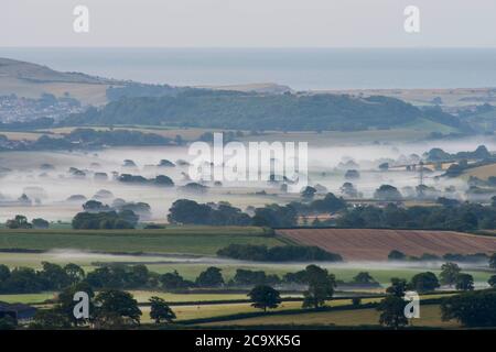Pilsdon Pen, Dorset, UK.  3rd August 2020.  UK Weather. Patches of mist in the Marshwood Vale viewed from Pilsdon Pen near Broadwindsor in Dorset at sunrise.  Picture Credit: Graham Hunt/Alamy Live News Stock Photo
