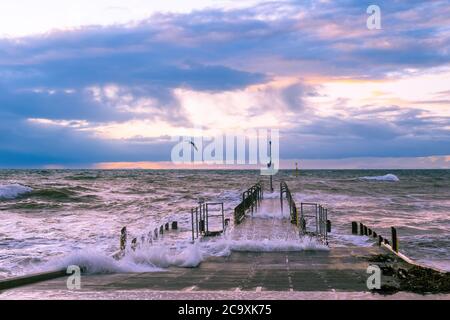 Beautiful sunset over foreshore with big waves and boat jetty Stock Photo
