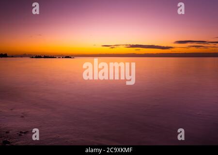 Vivid purple glowing sunset over smooth water and rock bird silhouettes Stock Photo