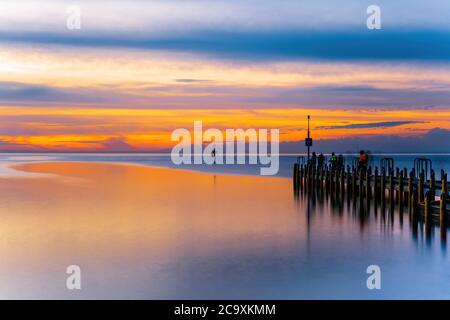 Vivid glowing orange sunset over ocean and boat jetty - long exposure seascape Stock Photo