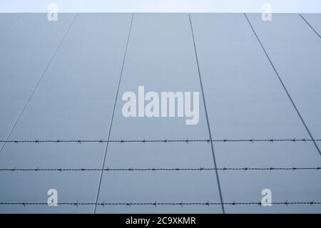Looking up at barbed wire against concrete wall with copy space Stock Photo