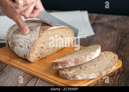 Close up of hands cutting a slice of bread. Male hands cutting bread on wooden board Stock Photo