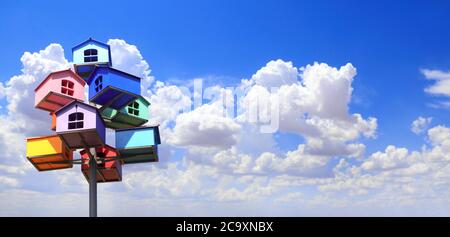 Horizontal banner with colorful nesting boxes on blue sky background. Many birdhouses of different colors and blue sky with clouds Stock Photo