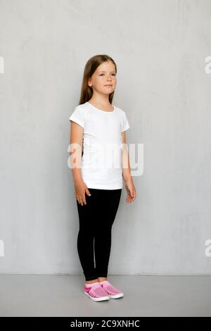 Little Cute Girl in White T-shirt and Black Leggings Sitting