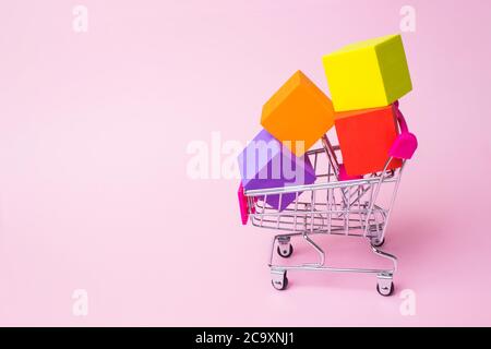 Close up toy metal shopping cart with red plastic handle and multicolor boxes inside on pink background. Big Sale and Discounts in Grocery. Best Price Stock Photo