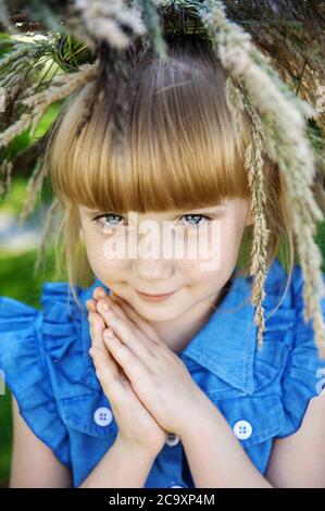beautiful red-haired girl with freckles and a wreath of summer herbs on her head looks into the camera with blue eyes. Young beautiful girl 7-10 years Stock Photo