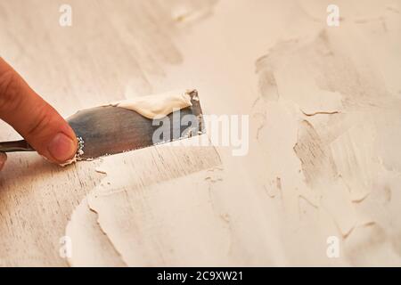 a small spatula applies putty to the wooden surface to create a structural background Stock Photo