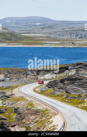 A red parcel delivery van on a curvy road in northern Norway in summer Stock Photo