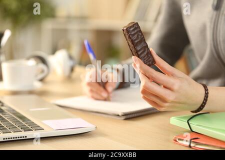 Close up of student girl hands holding chocolate snack bar studying at home