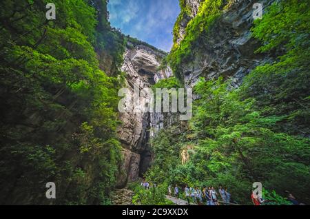 Wulong, China - August 2019 : Tourists walking on a sightseeing walking path going through the landscape of the massive vertical rock walls in Wulong Stock Photo