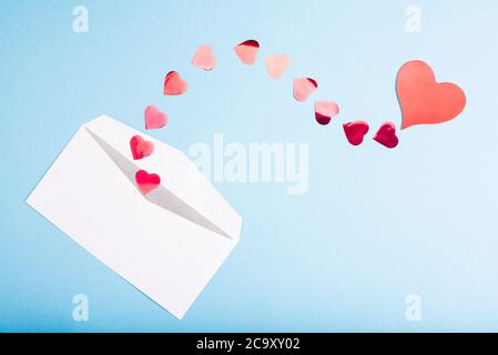 Red confetti hearts fly out of a white envelope on a light blue background. Valentine's Day. love concept Gift, message for lover Stock Photo