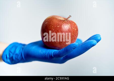 gloved hand holding a red apple, protection against coronavirus Stock Photo