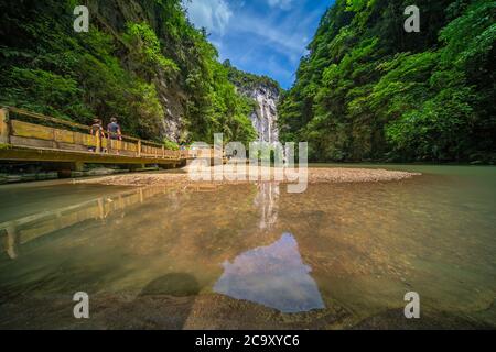 Wulong, China - August 2019 : Tourists walking on a wooden artificial bridge path along a river flowing through the landscape of the massive vertical Stock Photo