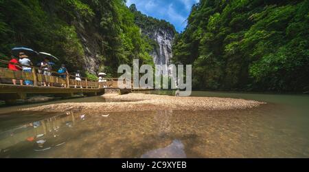 Wulong, China - August 2019 : Tourists walking on a wooden artificial bridge path along a river flowing through the landscape of the massive vertical Stock Photo