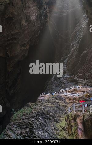 Wulong, China - August 2019 : Tourists climbing steps inside a stunning massive cave in a canyon among karst landscape of the Wulong National Park Stock Photo