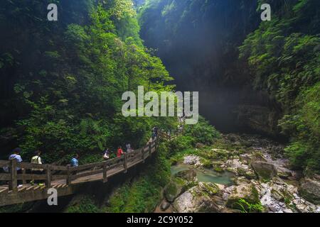 Wulong, China - August 2019 : Tourists walking on a wooden artificial walkway path going along the stream river flowing through the gorge and the land Stock Photo