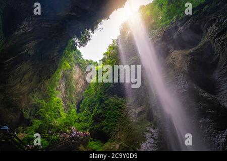 Wulong, China - August 2019 : Crowd of tourists walking on a narrow path under the Giant Waterfall in a valley gorge in the Longshuixia Fissure Nation Stock Photo