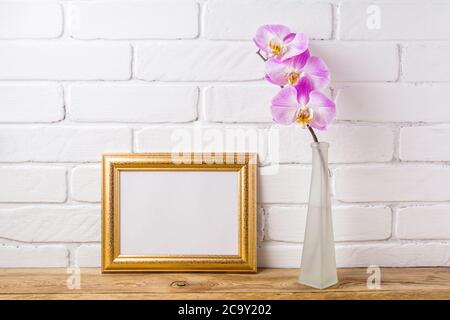 Gold decorated landscape, frame mockup with pink orchid in the matte glass vase. Empty frame mock up for presentation artwork. Template framing for mo Stock Photo