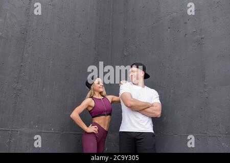 Smiling sportive caucasian couple in sportive clothes, wearing baseball caps posing over grey background, being happy with sport and love. Stock Photo