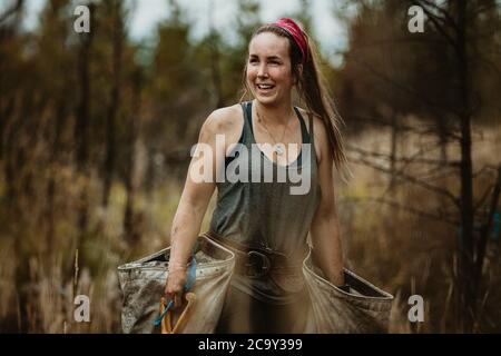 Female ranger planting trees in forest. Woman tree planter carrying bags full of trees. Stock Photo