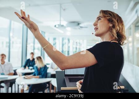 Businesswoman gesturing at projection screen and making a presentation to her colleagues in office. Female speaker giving presentation in conference. Stock Photo