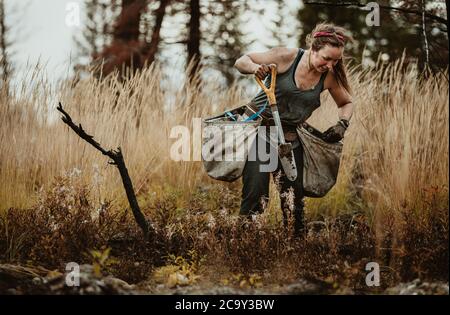 Woman digging hole in forest to plant saplings. Female planting new trees in forest. Stock Photo