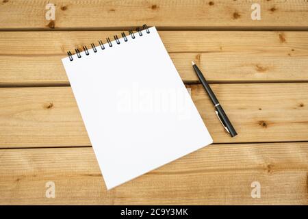 Open a blank notepad on the spiral on a wooden background with black pen. Stock Photo