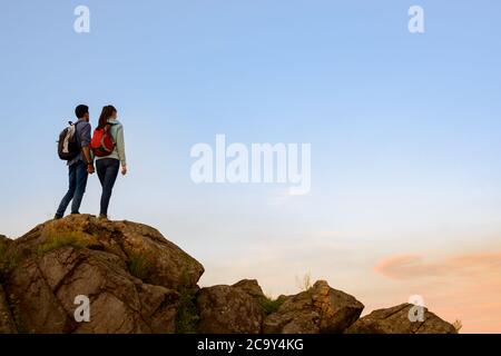 Couple of Young Travelers Standing on the Top of the Rock at Summer Sunset. Family Travel and Adventure Concept Stock Photo