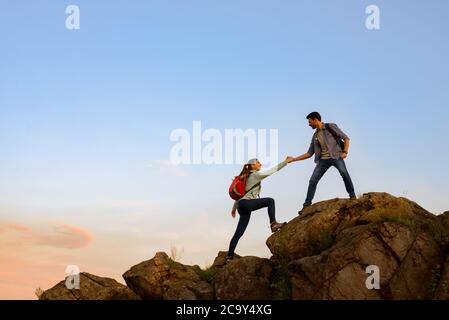 Travelers Hiking in the Mountains at Sunset. Man Helping Woman to Climb to the Top. Family Travel and Adventure. Stock Photo