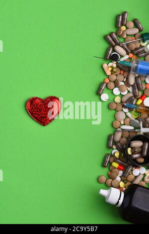 Set of colorful pills scattered on green background, copy space. Frame made of pills and capsules put in line. Drugs near syrup bottle, syringes, hear Stock Photo