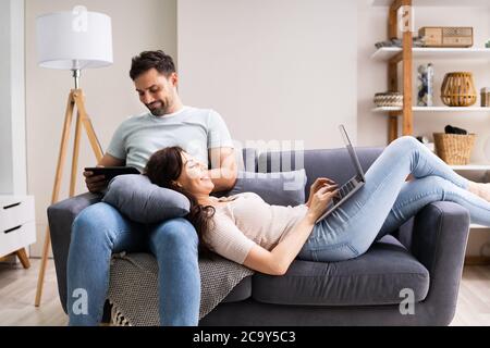Family Couple Using Laptop And Tablet On Couch Stock Photo