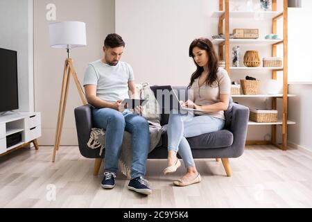 Family Couple Using Laptop And Tablet On Couch Stock Photo