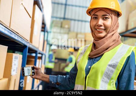 Portrait of Islam Muslim female warehouse worker use mobile phone scan qr code for online inventory in warehouse distribution environment. Using in bu Stock Photo
